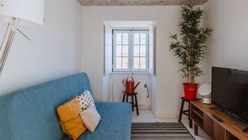 A living room with a blue sofa, a television, a potted plant, and a window with a view.