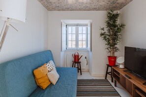 A living room with a blue sofa, a television, a potted plant, and a window with a view.