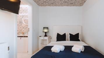 A hotel room with a bed, a nightstand with a lamp, a TV, and a bathroom visible through an open door.