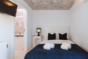A hotel room with a bed, a nightstand with a lamp, a TV, and a bathroom visible through an open door.