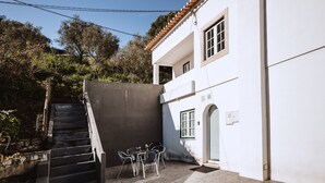 A white building with a tiled roof, a staircase leading to a door, and a small outdoor seating area with chairs and a table. - Encosta d'Óbidos T3 (Óbidos)