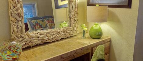 A bathroom with a wooden vanity, a mirror with a natural frame, a green vase, and a framed picture on the wall.