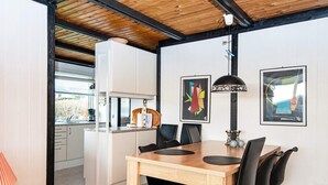 A modern kitchen with white cabinets, a wooden ceiling, and a dining area with a wooden table and black chairs.