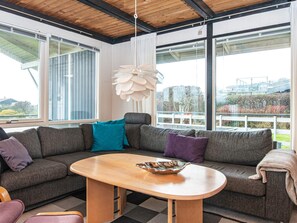 Ein modernes Wohnzimmer mit einem Ecksofa, einem Holztisch und großen Fenstern mit Blick ins Freie.