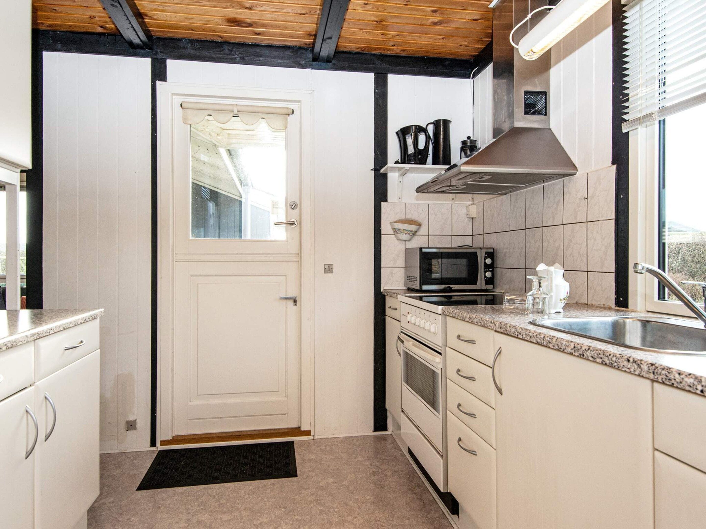 Una cocina con alacenas blancas, microondas, horno, pileta y ventana con persianas.