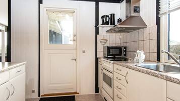Una cocina con alacenas blancas, microondas, horno, pileta y ventana con persianas.