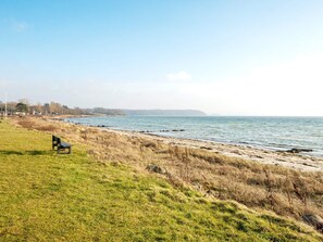 A grassy area with a bench overlooking a calm sea, a clear sky, and a distant shoreline with buildings. - 6 Person Holiday Home in Ronde (Ronde)