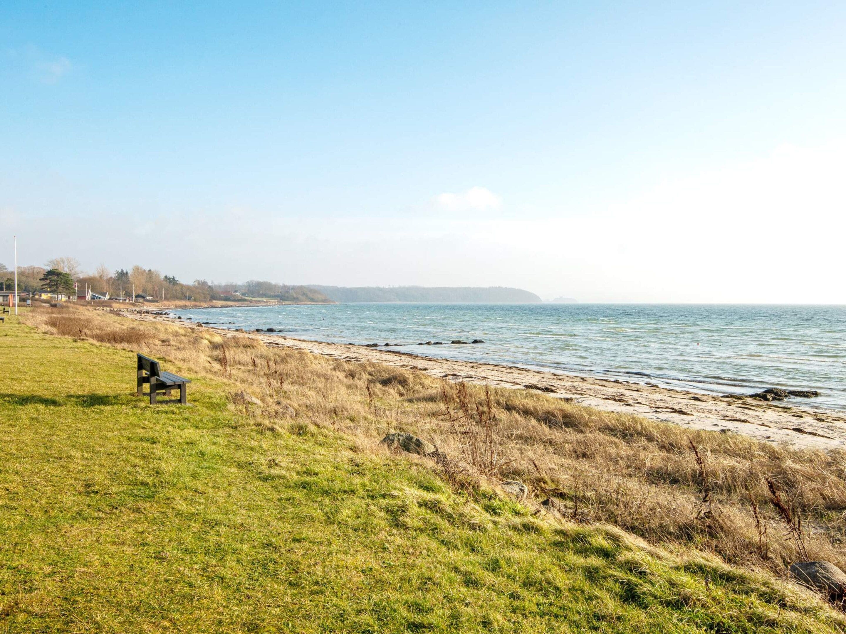 Un espace verdoyant avec un banc offrant une vue sur une mer calme, un ciel dégagé et une terre lointaine.