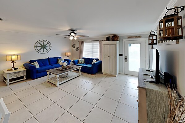 Ein Wohnzimmer mit zwei blauen Sofas, einem Couchtisch, einem Deckenventilator und einer weißen Tür mit einem Schild.