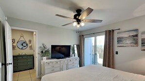 A bedroom with a bed, a TV, a ceiling fan, a dresser, and a sliding glass door.