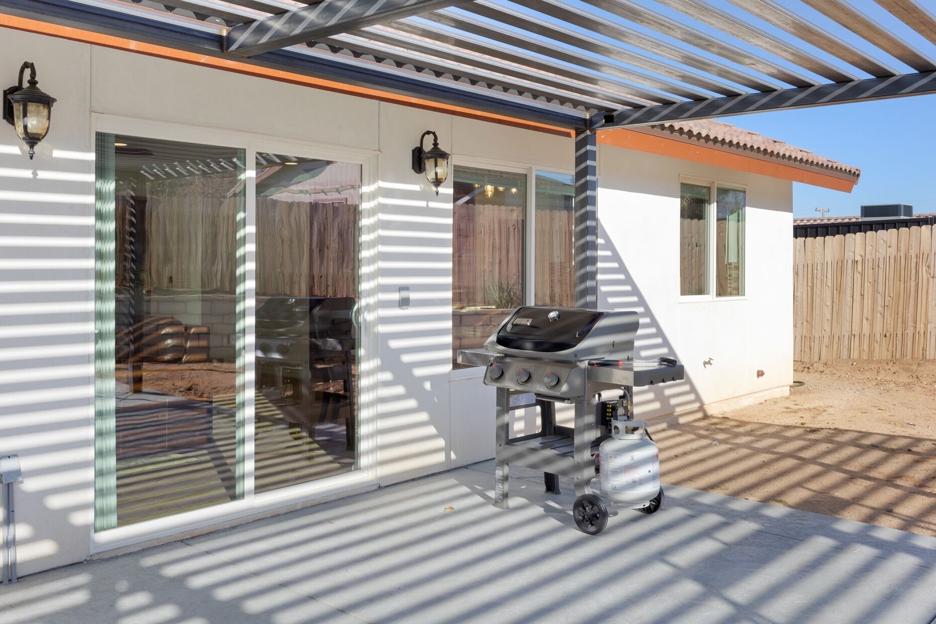 Eine überdachte Terrasse mit einem Grill, großen Schiebeglastüren und einem Holzzaun im Hintergrund.