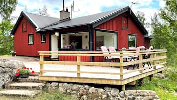 Una cabaña de madera roja con un balcón, escalones de piedra y una antena parabólica.