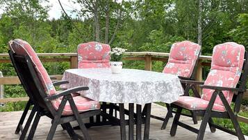 A round table with a floral tablecloth, surrounded by four chairs with floral upholstery, set on a wooden deck with a wooden railing.