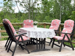A round table with a floral tablecloth, surrounded by four chairs with floral upholstery, set on a wooden deck with a wooden railing. - 4 Star Holiday Home in Ulrika (Ulrika)