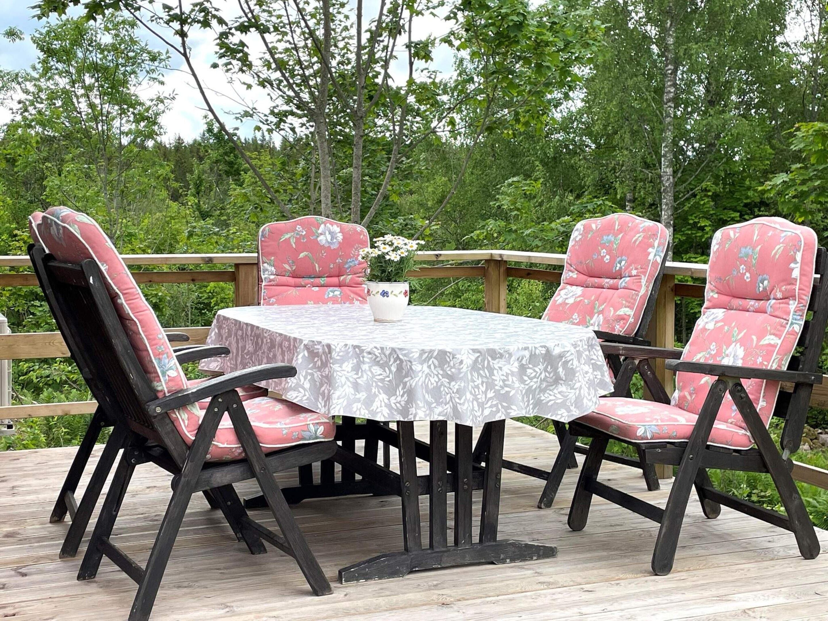 Una terraza de madera con una mesa redonda y cuatro sillas con tapicería floral.