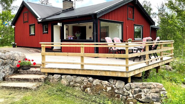 Une cabane en bois rouge avec une terrasse, des marches en pierre et une antenne parabolique.