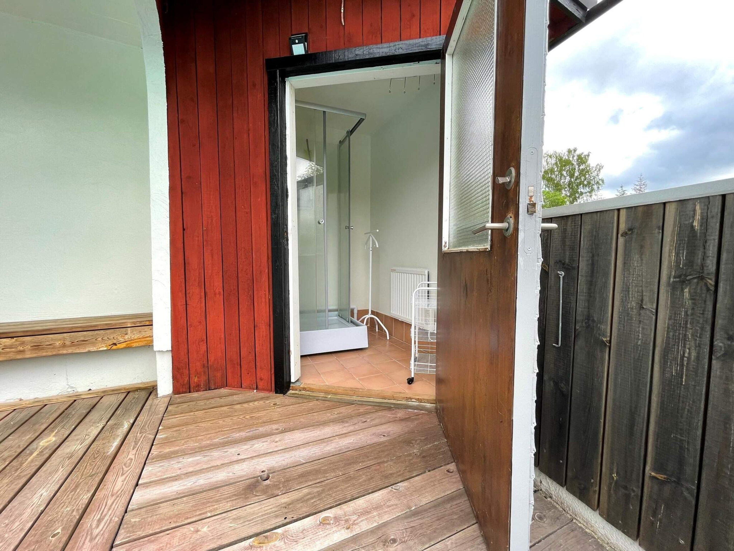 A wooden deck leading to a glass door opening into a room with a white radiator and a white chair.