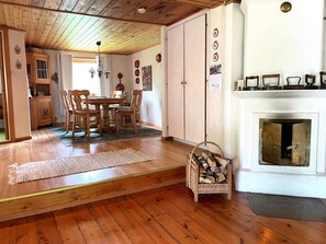 A wooden-floored room with a dining table and chairs, a fireplace, and a wall with decorative plates. - 4 Star Holiday Home in Ulrika (Ulrika)