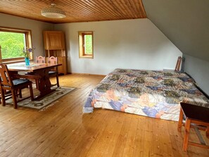 Una habitación con techo de madera, una cama con colcha floral, una mesa de comedor con sillas y una ventana con vistas a follaje.