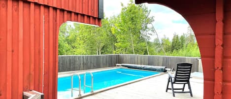 A wooden deck with a swimming pool, a covered area, and a chair.
