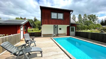 A wooden deck with a swimming pool, a red building, and a clear sky.