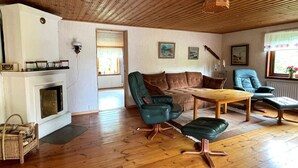 Un salon avec une cheminée, un plancher en bois, un canapé, une table basse et une fenêtre avec des rideaux.