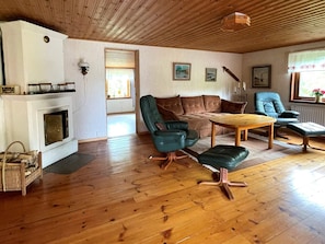 A living room with a fireplace, wooden flooring, a sofa, a coffee table, and a window with curtains. - 4 Star Holiday Home in Ulrika (Ulrika)