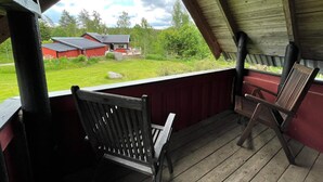 Une véranda couverte avec des chaises en bois, donnant sur une grange rouge et un paysage verdoyant.