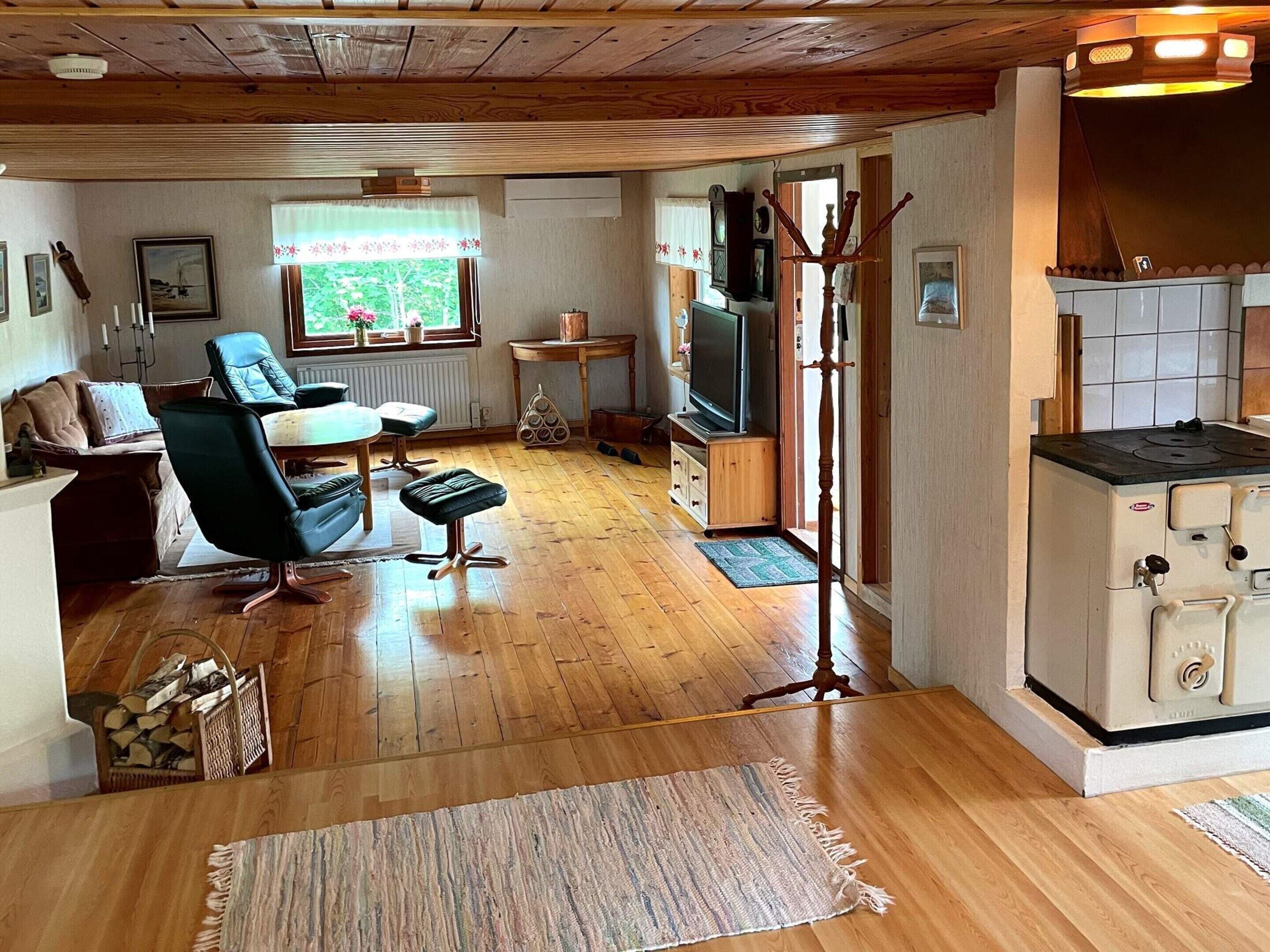A cozy living room with a wooden floor, a sofa, a chair, a television, and a kitchen area with a stove.