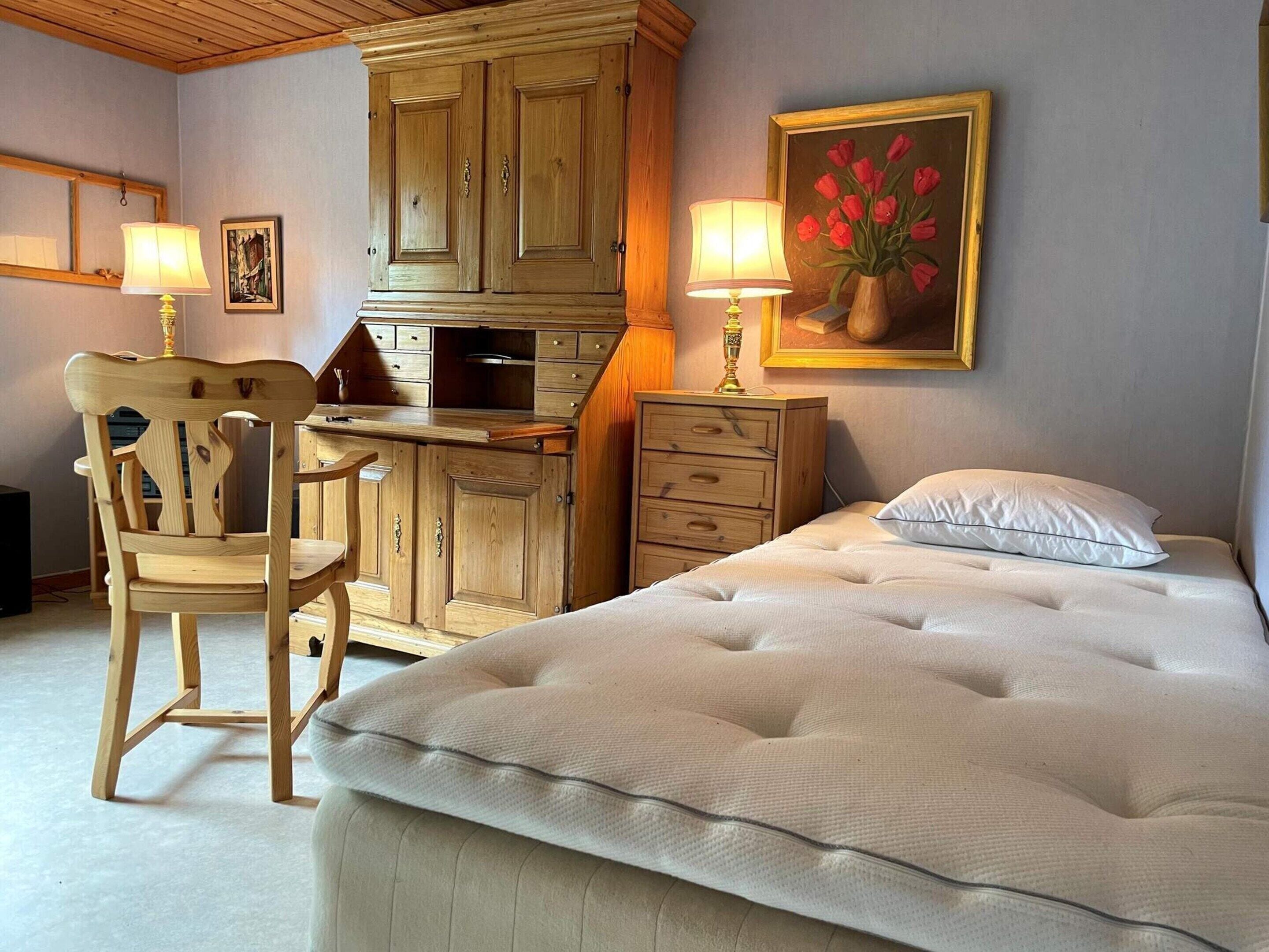 A bedroom with a bed, a wooden desk, a chair, and a dresser.