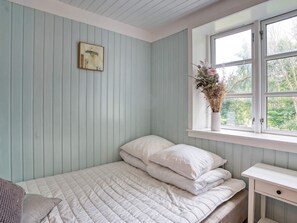 A bedroom with a bed, a bedside table, a window with a view of greenery, and a wall-mounted picture. - 6 Person Holiday Home in Melby (Melby)