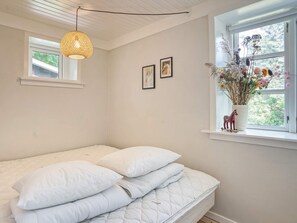 Une chambre à coucher avec un lit, une fenêtre donnant sur un beau paysage, un luminaire suspendu et un vase rempli de fleurs placé sur le rebord de la fenêtre.