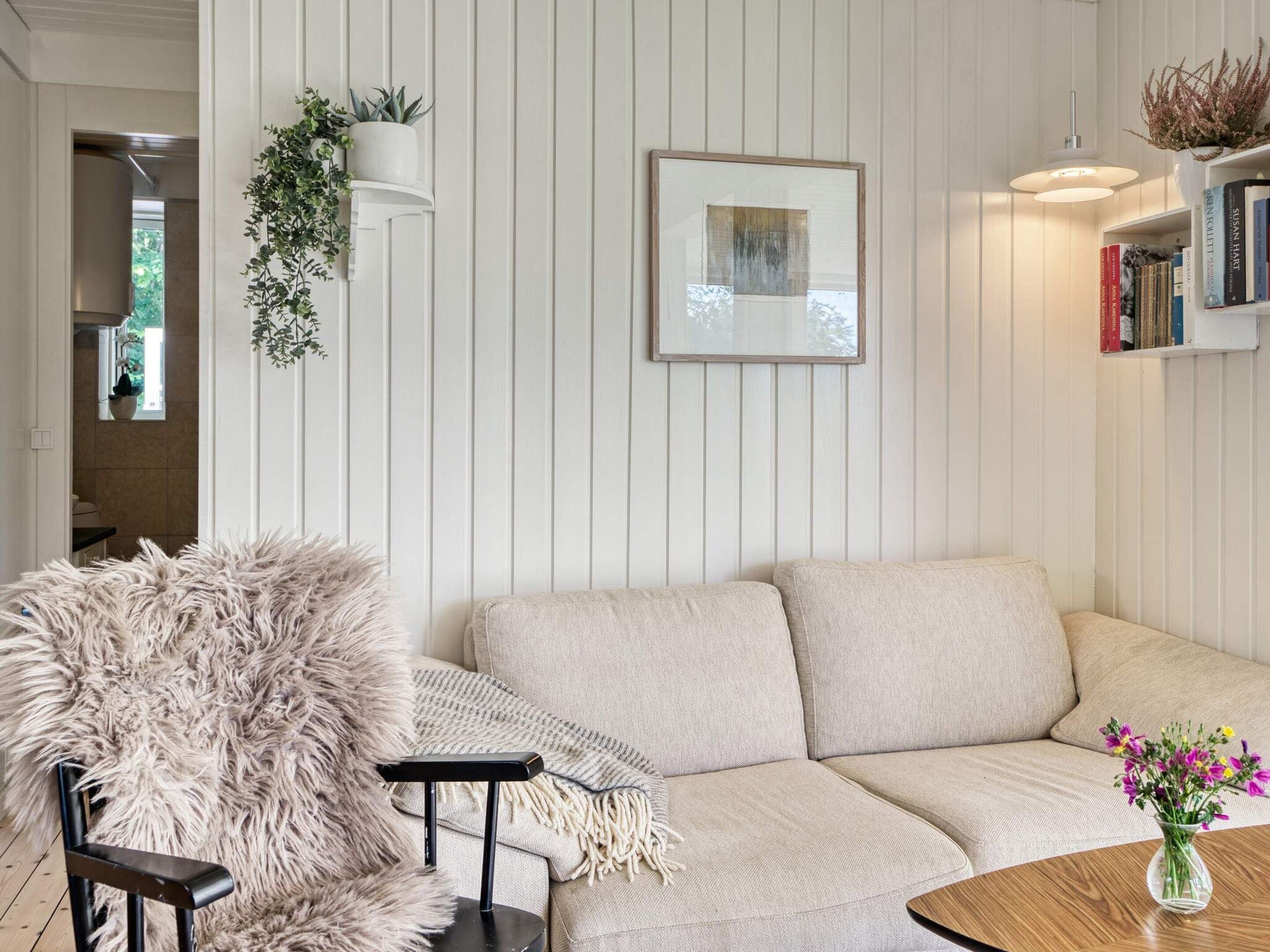 En stue med en sofa, en fluffy lænestol, et lille bord med en vase blomster og en reol fyldt med bøger.