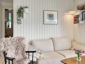 A living room with a sofa, a furry chair, a small table with a vase of flowers, and a bookshelf with books. - 6 Person Holiday Home in Melby (Melby)