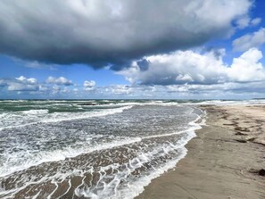 Una playa con olas, cielo nublado y horizonte despejado.