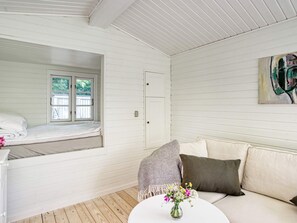 Et værelse med en seng, en sofa, et lille bord med en blomstervase og en dør til et andet rum.