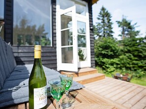 En flaske hvid Moscato vin, to glas med grøn væske, og et træterrasse med en bænk.