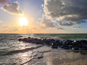 Uma praia com ondas, rochas e um pôr do sol.