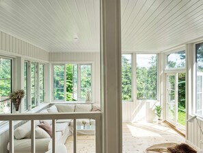 Una habitación con techo de madera blanca, ventanas grandes, un sofá blanco y una mesita con un florero.