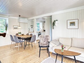 A modern interior with a dining area, sofa, and a kitchen visible through an open doorway.