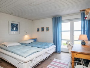 Ett rum med en säng, ett skrivbord, en stol, en lampa och ett fönster med gardiner.