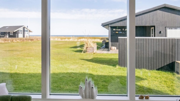 A room with a large window overlooking a grassy field and a building with a sloped roof.
