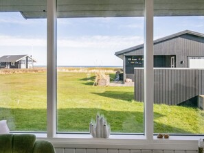 A room with a large window overlooking a grassy field and a building with a sloped roof.
