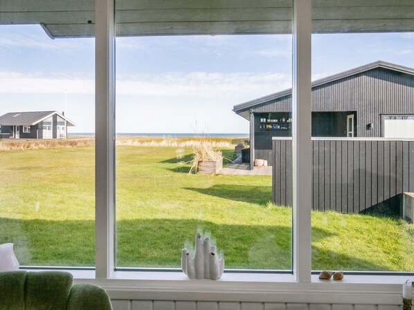 A room with a large window overlooking a grassy field and a building with a sloped roof.