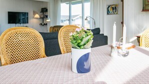 A dining area with a table set for two, a wicker chair, a sofa, and a television mounted on the wall.