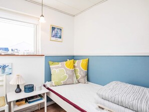 A bedroom with a bed, a bedside table, a lamp, a picture frame, and a window with a view.