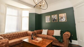 A living room with a sectional sofa, a wooden coffee table, and a chandelier. - By the Tracks (Buxton)
