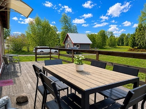 Une terrasse en bois avec une table et des chaises, un petit abri de jardin et une voiture garée à proximité.