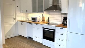 Moderni keittiö, jossa on valkoiset kaapit, mikroaaltouuni, kahvinkeitin ja uuni.