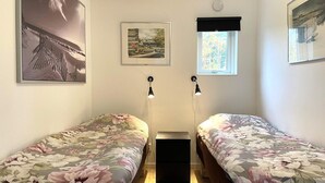 Makuuhuoneessa on kaksi erillistä sänkyä, yöpöytä, ikkuna, josta on näkymä, ja kaksi seinälle asennettua lamppua.